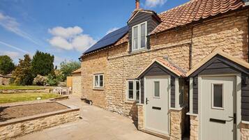 A stone house with a tiled roof, a solar panel, and a paved patio.
