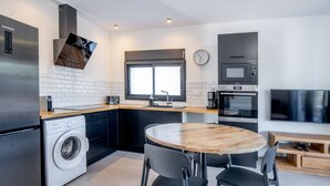 A modern kitchen with a built-in washing machine, a dining area with a round table and chairs, and a TV mounted on the wall. - House with AC and WiFi - 2 guests, near St-Pierre (Saint-Pierre)