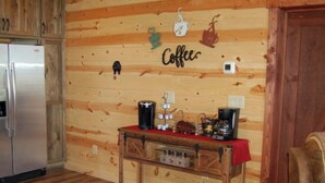 Ein Holzinterieur mit einer Kaffeethematik an der Wand, einem Kühlschrank, einem Holztisch mit Kaffeemaschinen und einem Stuhl.