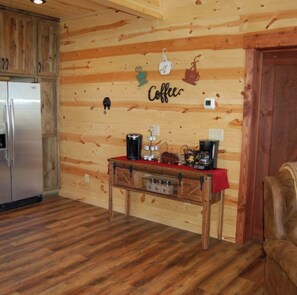 Ein Holzinterieur mit einer Kaffeethematik an der Wand, einem Kühlschrank, einem Holztisch mit Kaffeemaschinen und einem Stuhl.