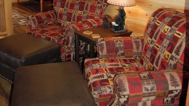 Ein Holzblockhaus-Innenraum mit einer Sofagarnitur, einem Tisch mit einer Lampe und einem Ledersitzhocker.