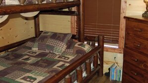Ein Etagenbett mit Decke, einem Holz-Kopfteil und einem Fenster mit Jalousien.