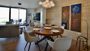 A modern dining area with a round table, chairs, and a television on the wall. - Modern duplex, panoramic view - 6 guests (Évian-les-Bains)