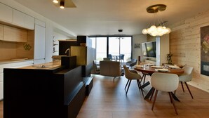 A modern kitchen with a central island, a dining area with a round table and chairs, and a living space with a large TV. - Modern duplex, panoramic view - 6 guests (Évian-les-Bains)
