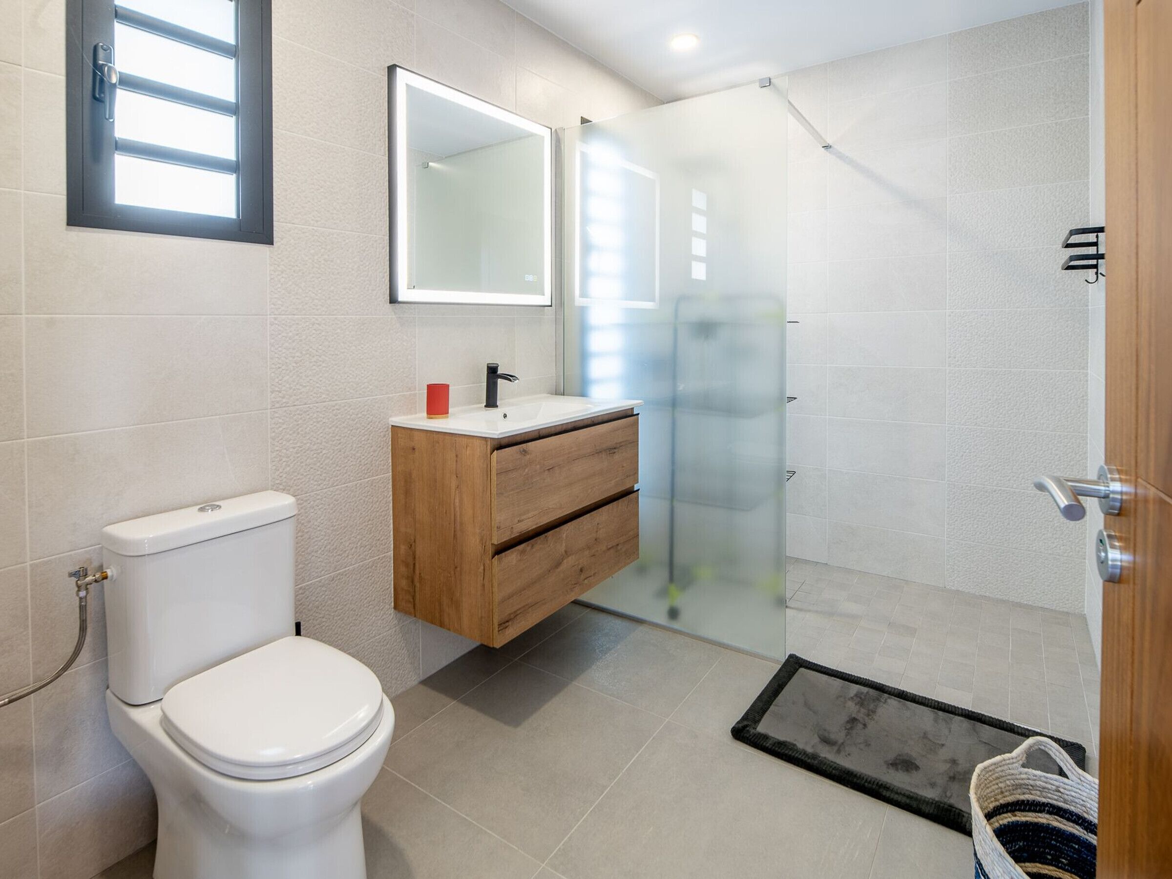 Une salle de bain moderne comprenant des toilettes, un meuble-lavabo en bois, une cabine de douche en verre et un miroir.