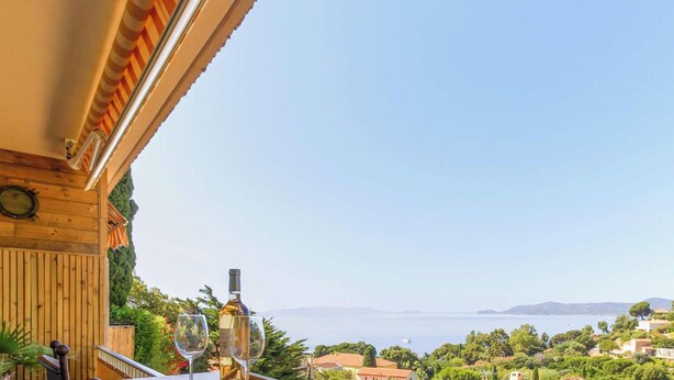 A wooden balcony with a view of a coastal town and the sea. - Apartment, pets welcome, sea view - 4 guests (Le Lavandou)