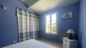 Ein Schlafzimmer mit einem Bett, einem Fenster, einem Nachttisch und einer Lampe.