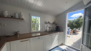 Eine moderne Küche mit weißen Schränken, einer Holzausziehtafel, einer Kaffeemaschine und Blick ins Freie.