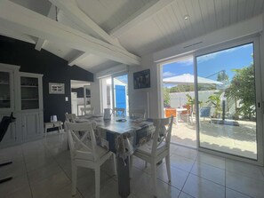 A spacious dining area with a large table and chairs, a kitchen with cabinets, and a sliding glass door leading to an outdoor patio. - Cozy house near the beach - 8 guests (L'Épine)