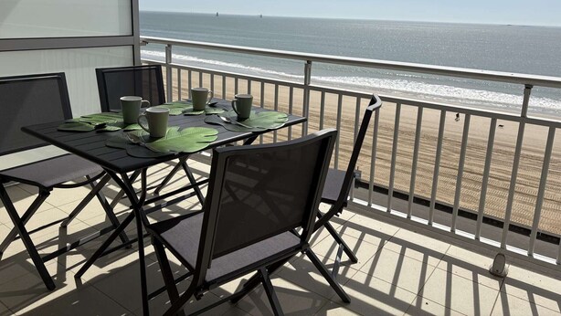 Ein Balkon mit Tisch für zwei Personen mit Blick auf einen Strand.
