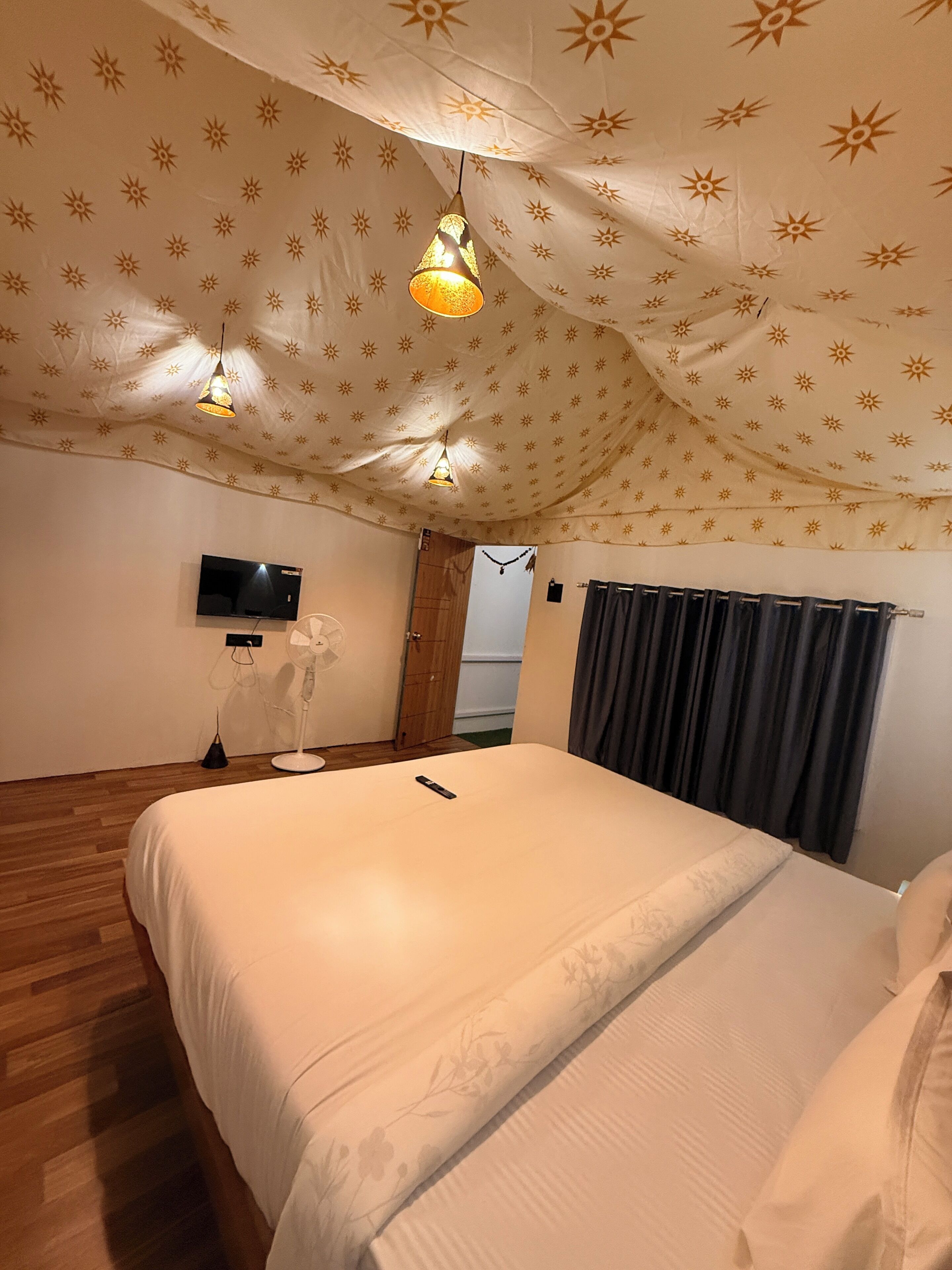 Camera da letto con un letto, una TV, un ventilatore e un soffitto decorato con un motivo solare.
