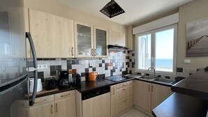 Eine moderne Küche mit hellen Holzschränken, einer schwarzen Arbeitsplatte und Meerblick durch ein Fenster.