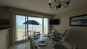 Ein Essbereich mit Blick auf den Strand, ein an der Wand befestigter Fernseher und eine Kristallleuchter.
