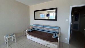 Ein Schlafzimmer mit einem Bett, einem kleinen Tisch, einem Spiegel und einer Tür zu einem weiteren Raum.