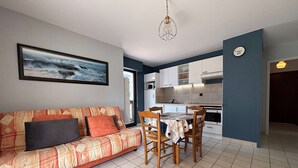 Ein Wohnzimmer mit Sofa, einem Esstisch mit Stühlen, einer Küchenzeile und einem großen Gemälde an der Wand.