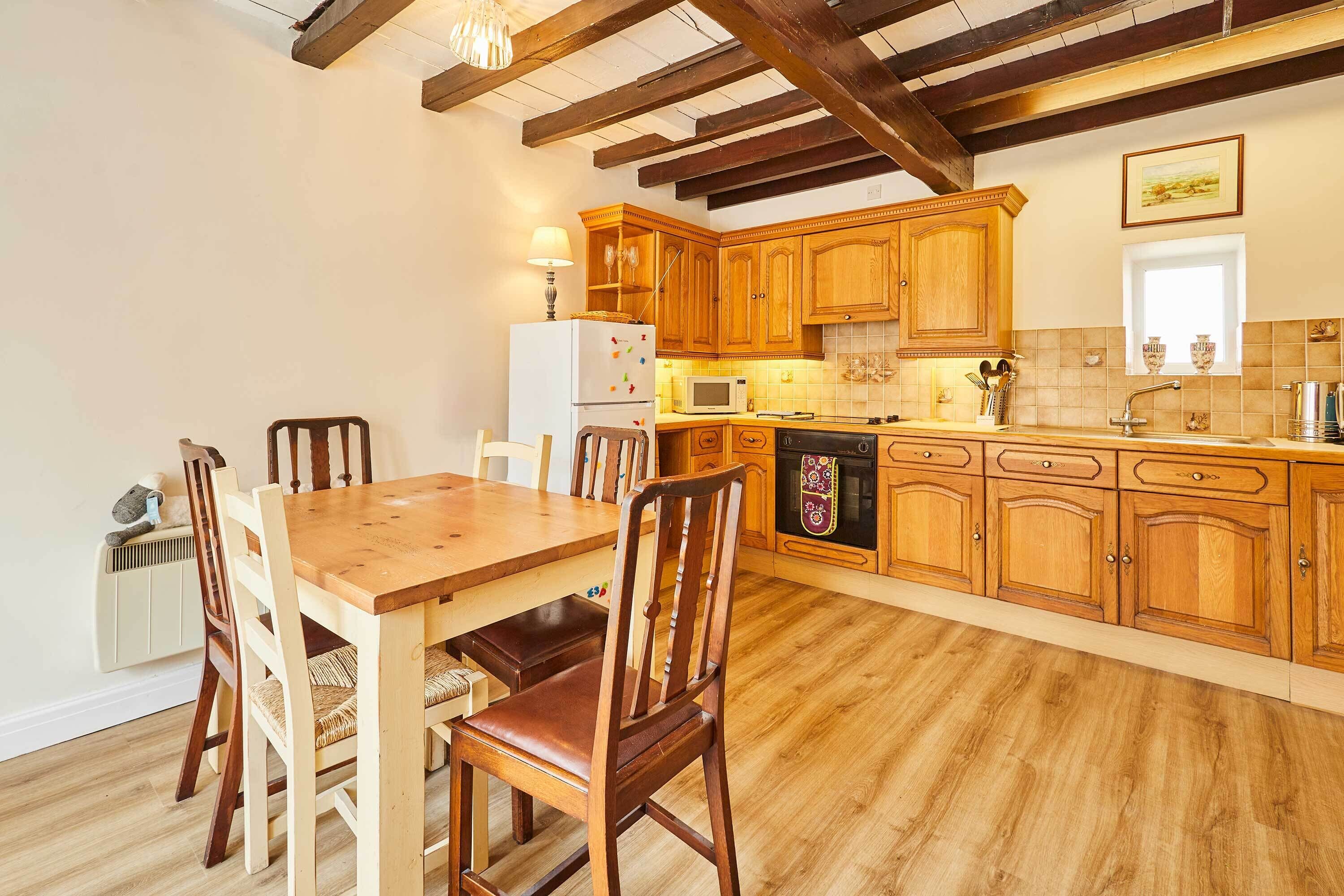 Une cuisine avec des meubles en bois, une table à manger, des chaises, un réfrigérateur, un four à micro-ondes et un lave-vaisselle.
