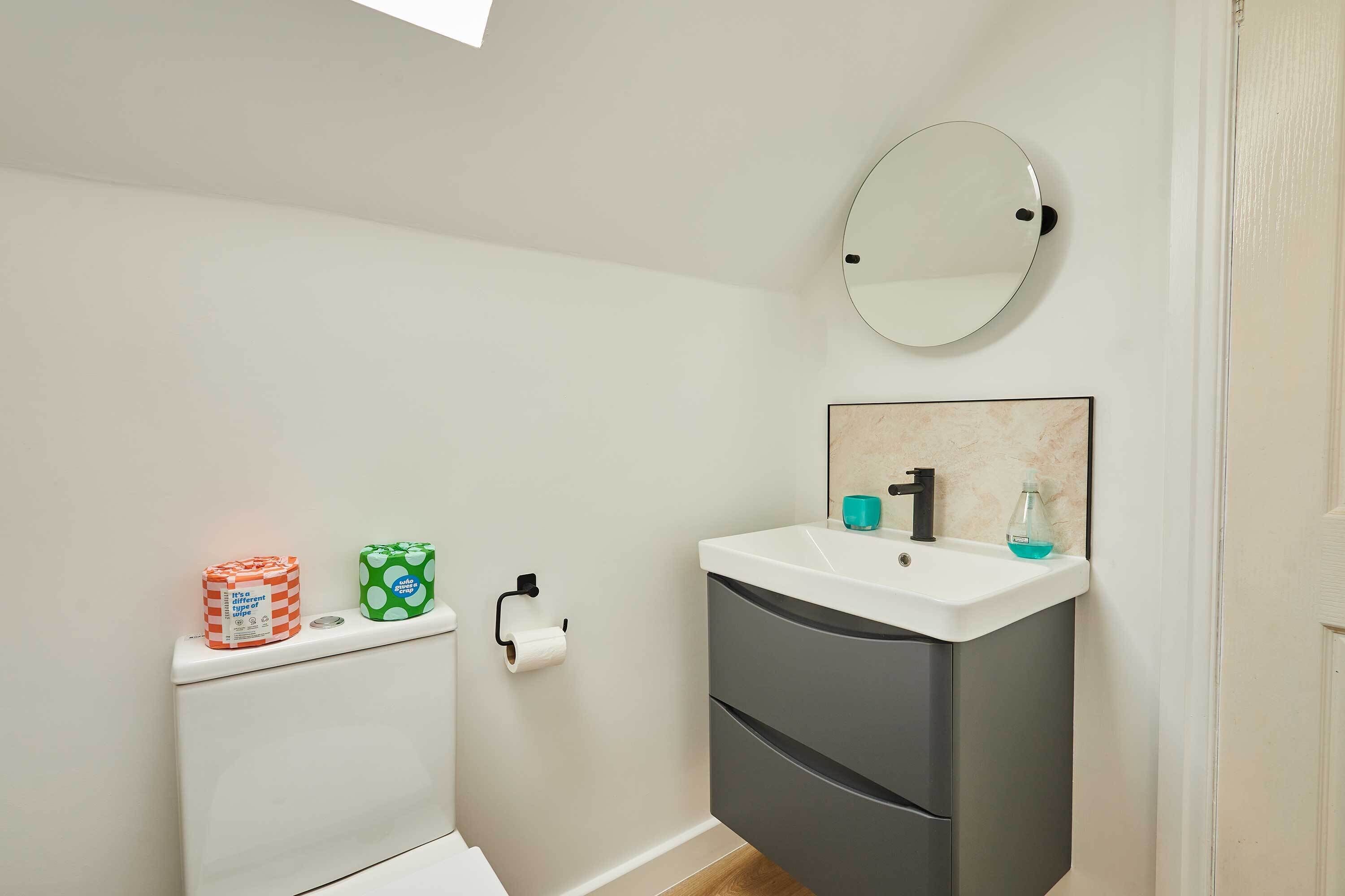 A bathroom with a toilet, a sink with a mirror, and a toilet paper holder.