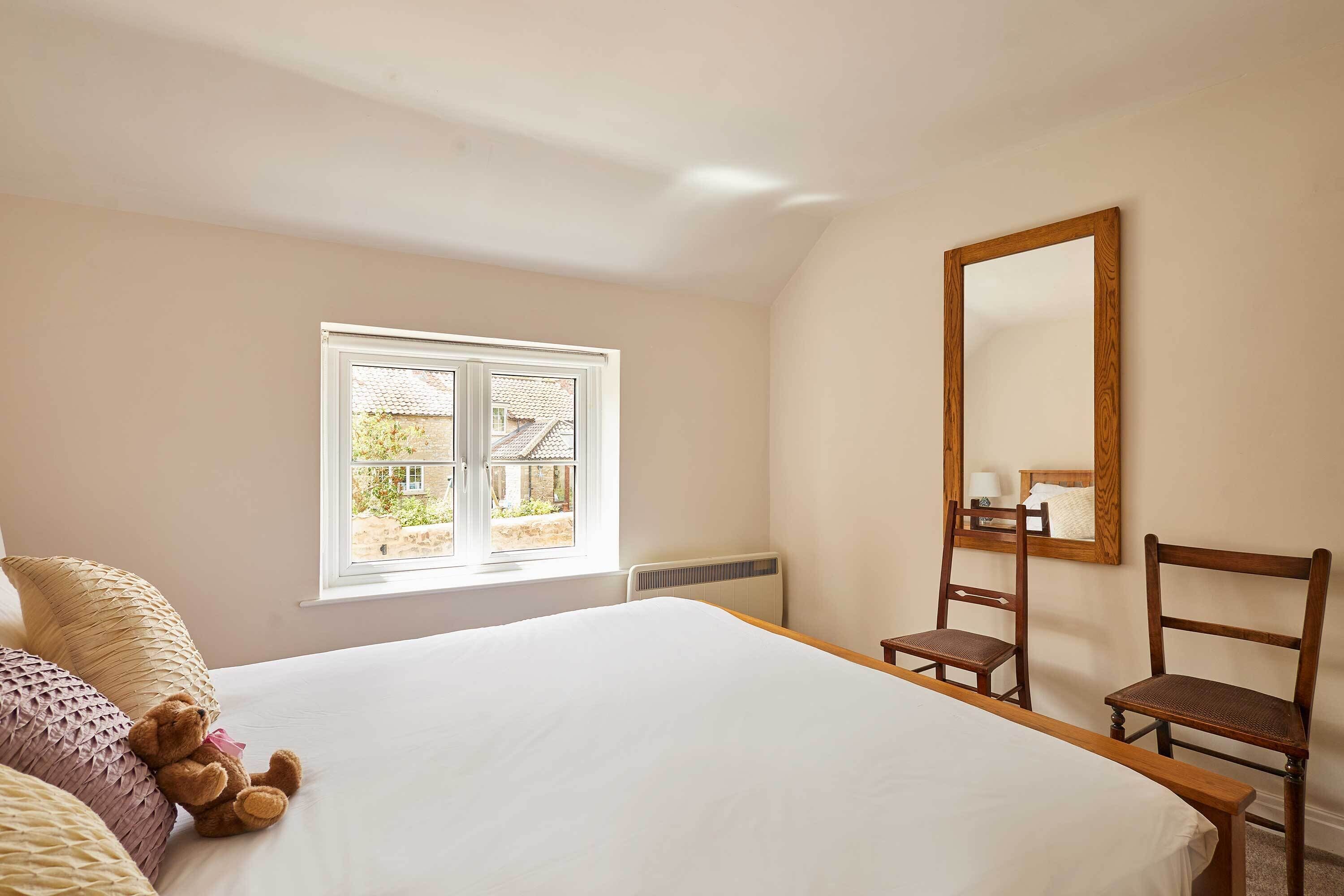 Une chambre à coucher avec un lit, une chaise, une fenêtre et un miroir.