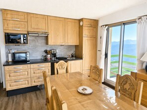 A compact kitchen with wooden cabinets, a microwave, and a dining table with chairs. - Apartment with mountain view - 8 guests (Saint-Lary-Soulan)