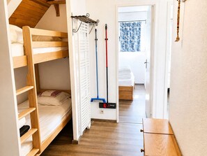 Una cama litera con escalera de madera, un radiador, una escoba y una puerta que da a otra habitación.