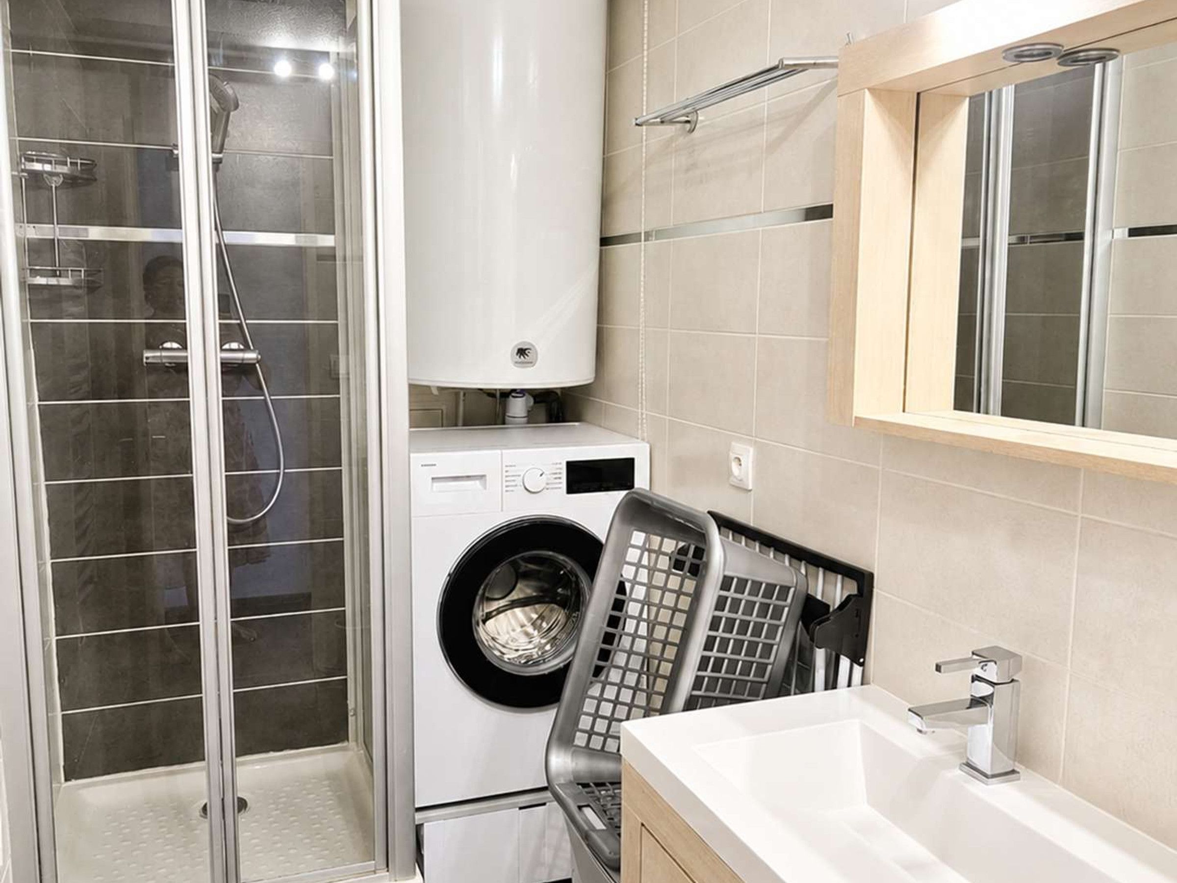 Een moderne badkamer met een douchecabine van glas, een wasmachine met voorlaadopening en een wastafel met spiegel erboven.