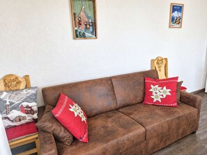 A brown sofa with red and white pillows, a wooden headboard, and a small table with a red cushion. - Apartment with mountain view - 8 guests (Saint-Lary-Soulan)
