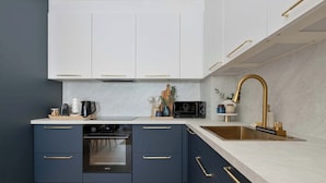 A modern kitchen with dark blue cabinets, a white countertop, a stainless steel sink, and a gold faucet. - Luxury Apartment with a Balcony | Balcony (Władysławowo)