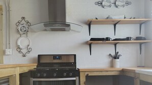 Une cuisine compacte équipée d’une cuisinière, d’un four et d’étagères en bois.