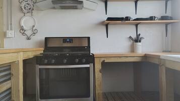 A compact kitchen with a stove, oven, and wooden shelves.