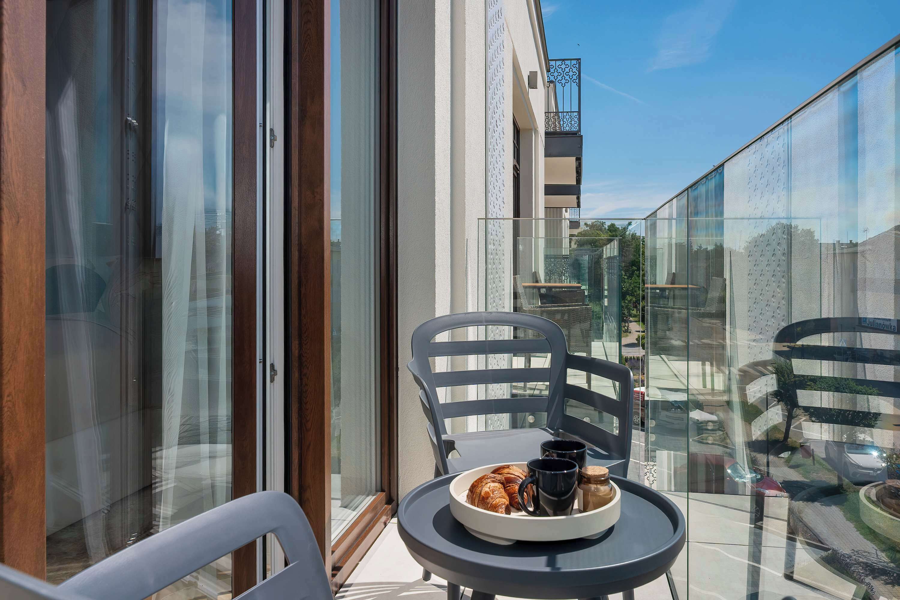 Un balcon avec une table, des chaises et un plateau contenant des croissants et des tasses de café.