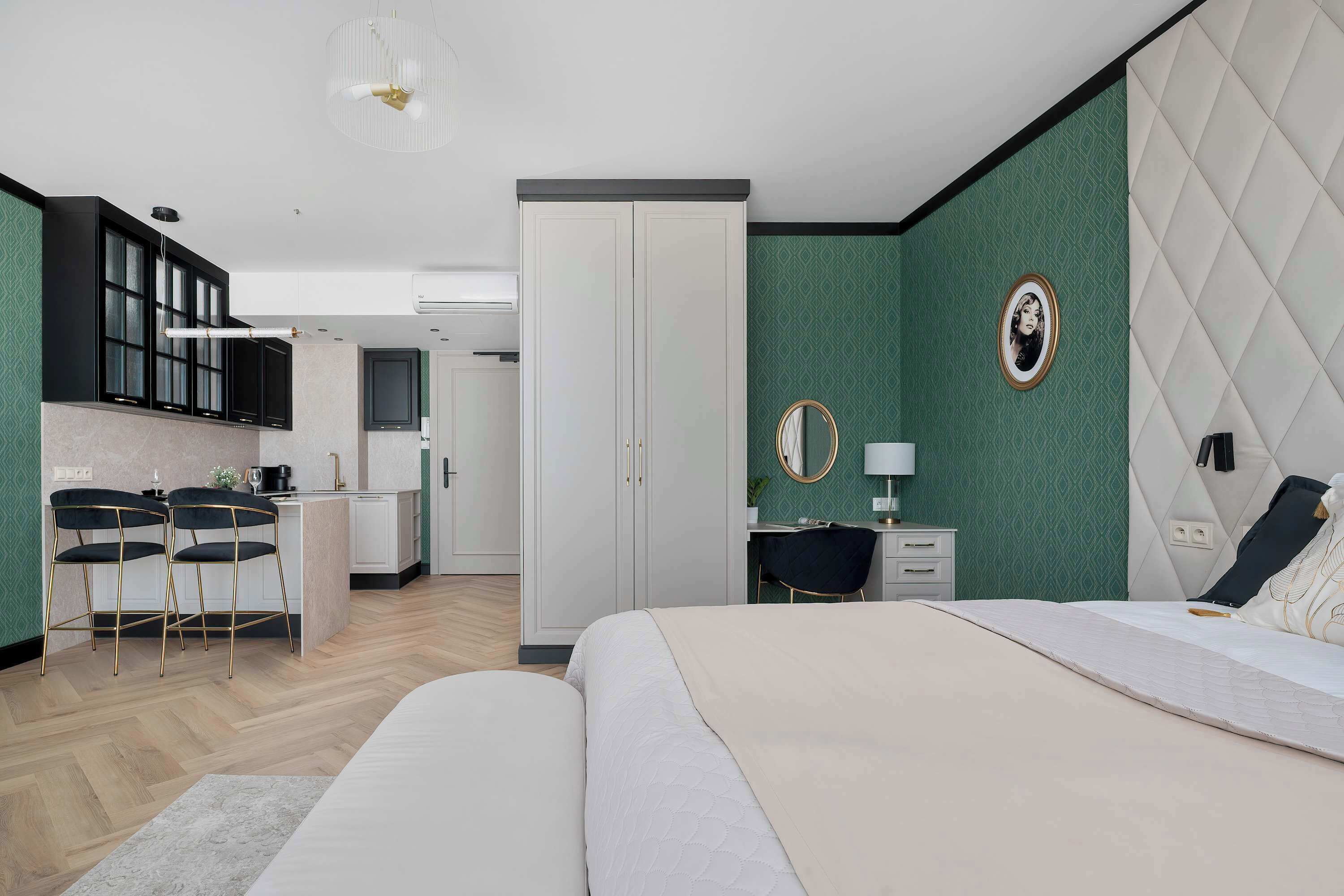 A modern hotel room with a bed, a desk, and a kitchenette.