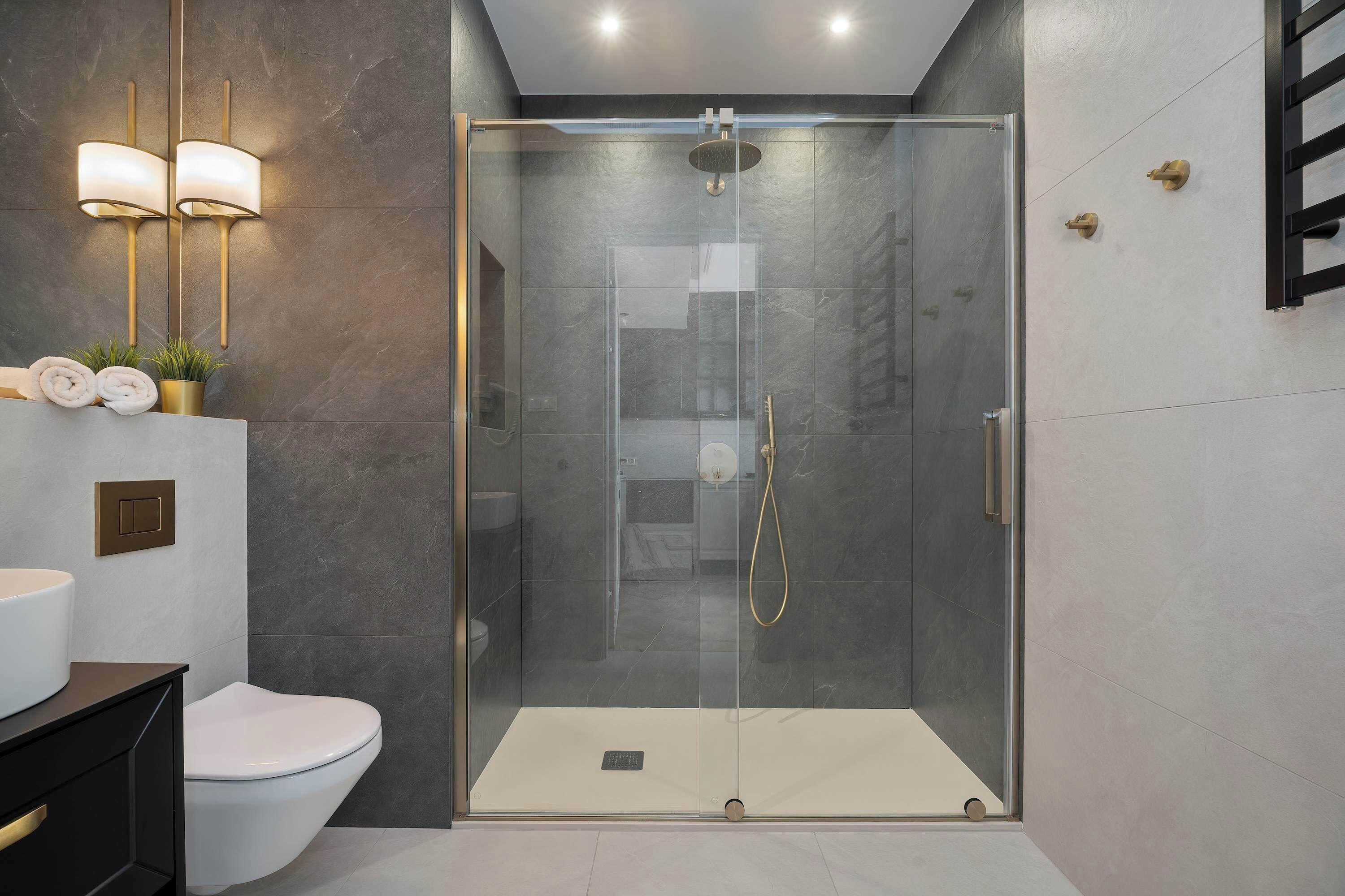 Une salle de bain moderne avec une douche à parois de verre, des toilettes blanches et un lavabo doté d’un robinet doré.