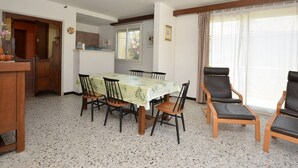 A dining area with a table, chairs, a kitchen in the background, and a window with curtains. - Apartment with parking - 6 guests (Le Grau-du-Roi)