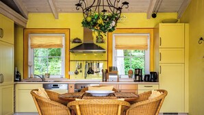 A yellow kitchen with wicker chairs, a dining table, and a hanging light fixture. - Kathi Vacation Home on Lake Jabelschen with a Garden, Terrace, and Fireplace (Jabel)