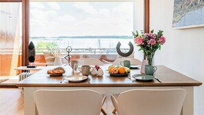 Ein Esstisch mit Tellern, Tassen und einer Blumenvase, mit Blick auf ein Gewässer.
