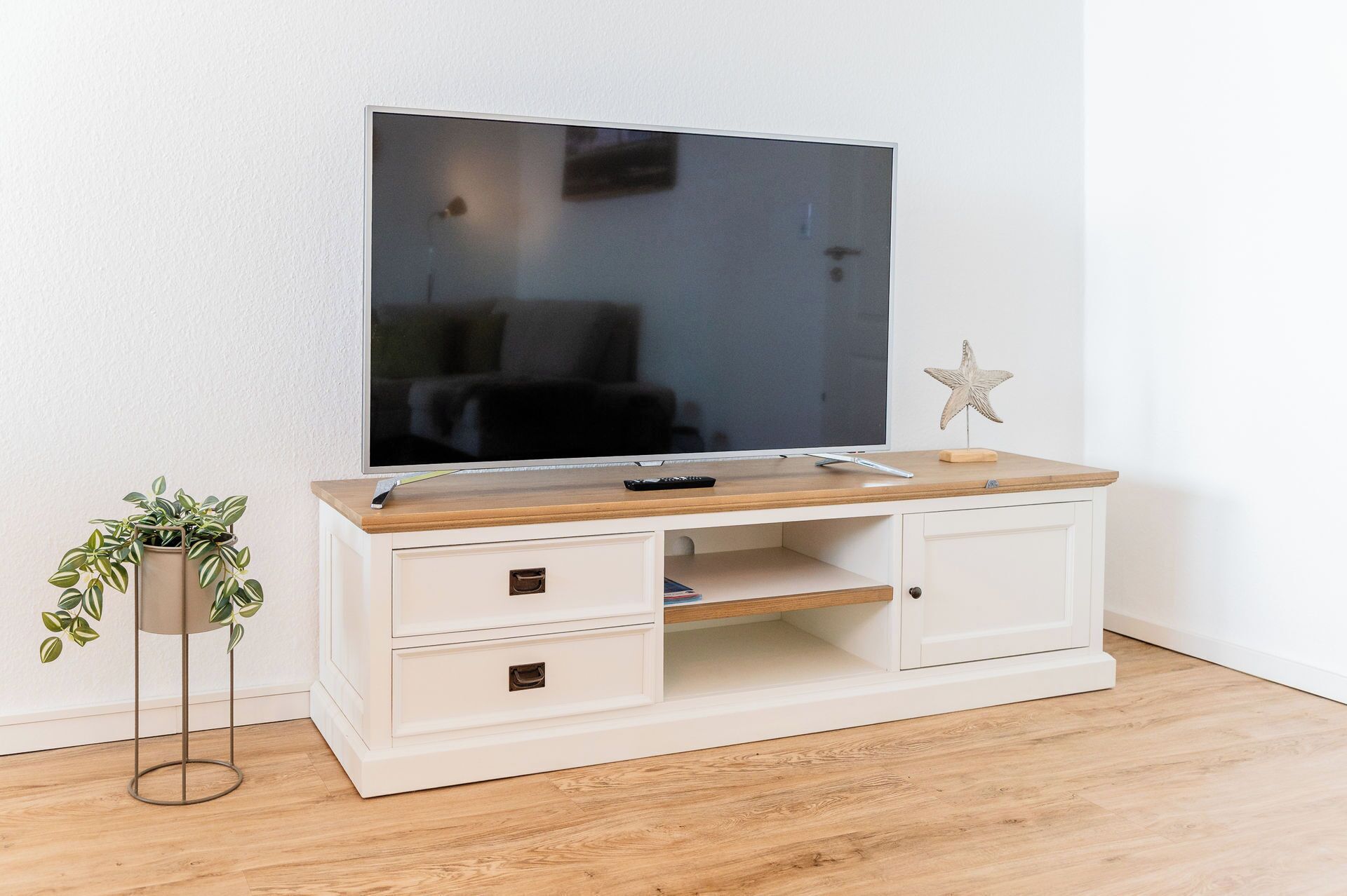 Een televisie op een houten tv-meubel met lades, een klein plantje en een ster decoratie.