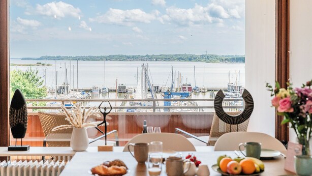 Ein Essbereich mit Blick auf eine Marina, ein Tisch mit Frühstücksangeboten und ein dekorativer Spiegel.