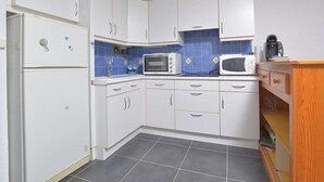 Een keuken met witte kastjes, twee magnetrons en een koelkast.