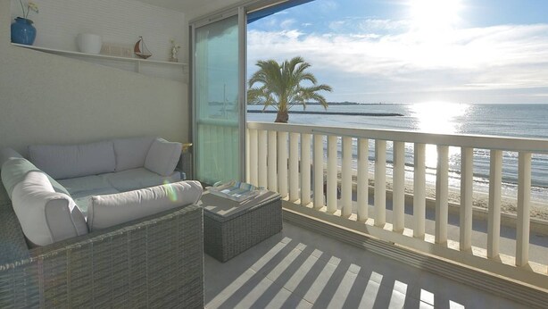 Een balkon met een witte reling, een rieten bank en een kleine tafel.