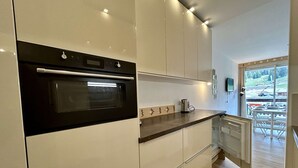 Una cuina moderna amb forn integrat, cafetera i vista a un solar en construcció a través d'un gran finestral.