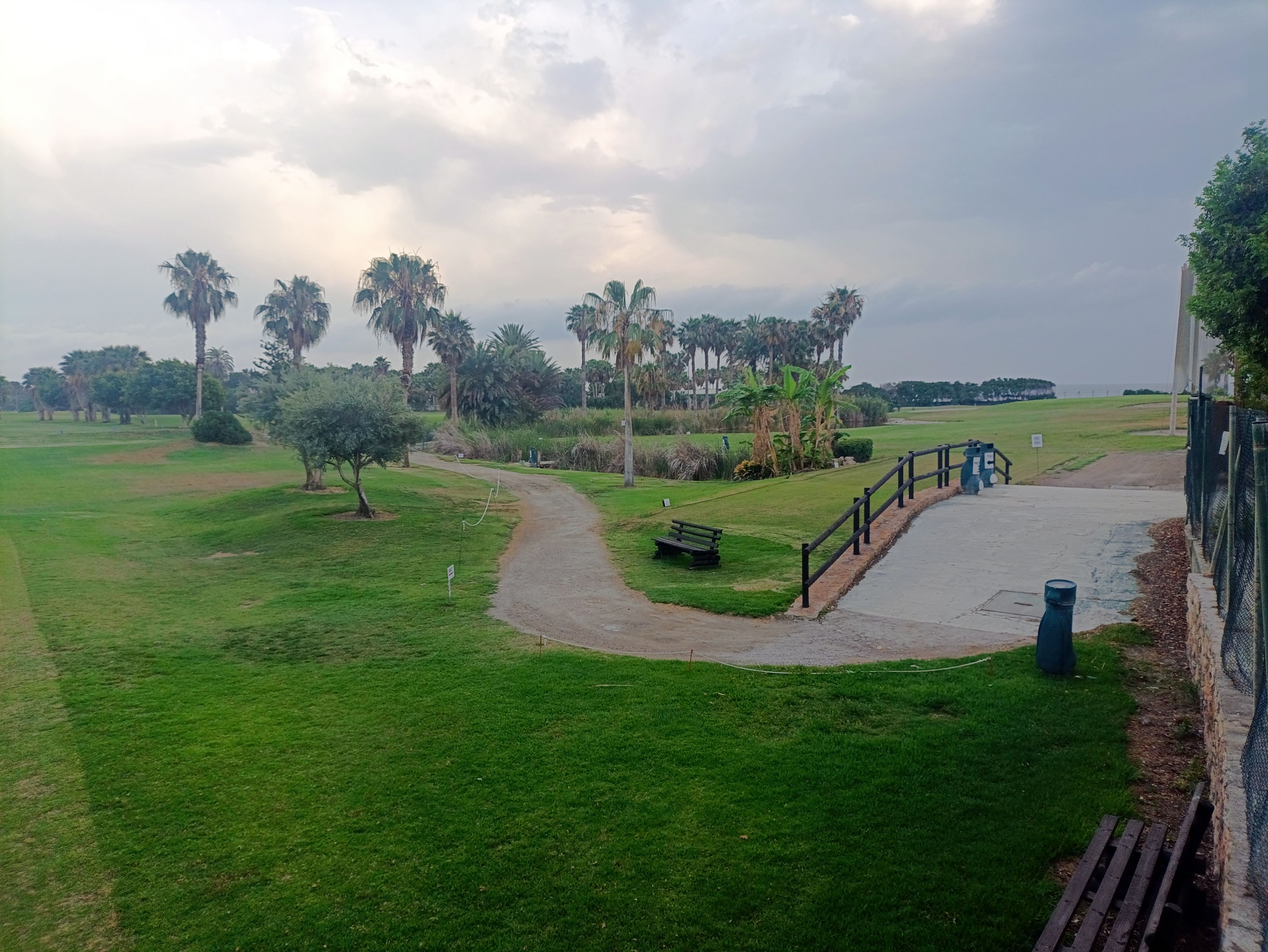 A pathway leading to a gated area with a bench and a fence.