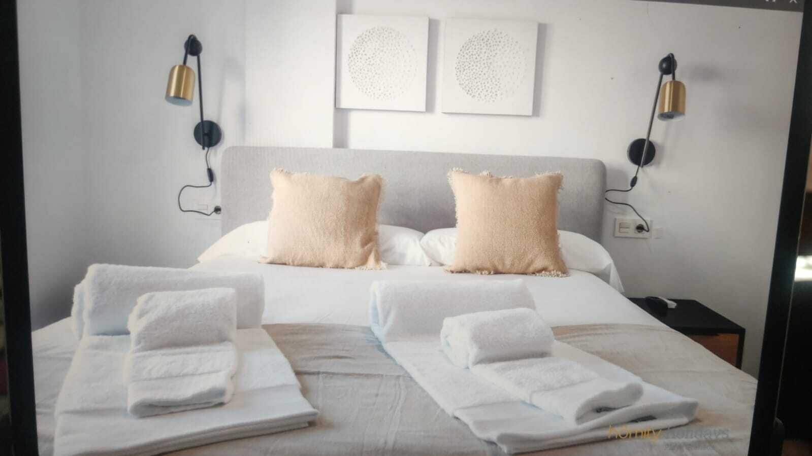 A hotel room with a bed, two pillows, two bedside lamps, and two towels on the bed.