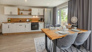Una cuina moderna amb armaris blancs, un taulell de fusta i una zona de dinar amb taula de fusta i cadires grises.