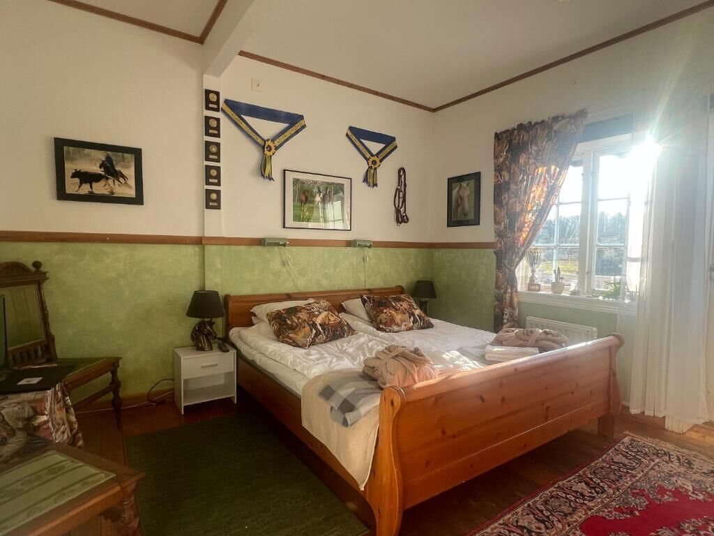 Um quarto com uma cama de madeira, uma mesa de cabeceira, uma luminária, um quadro emoldurado e uma janela com cortinas.
