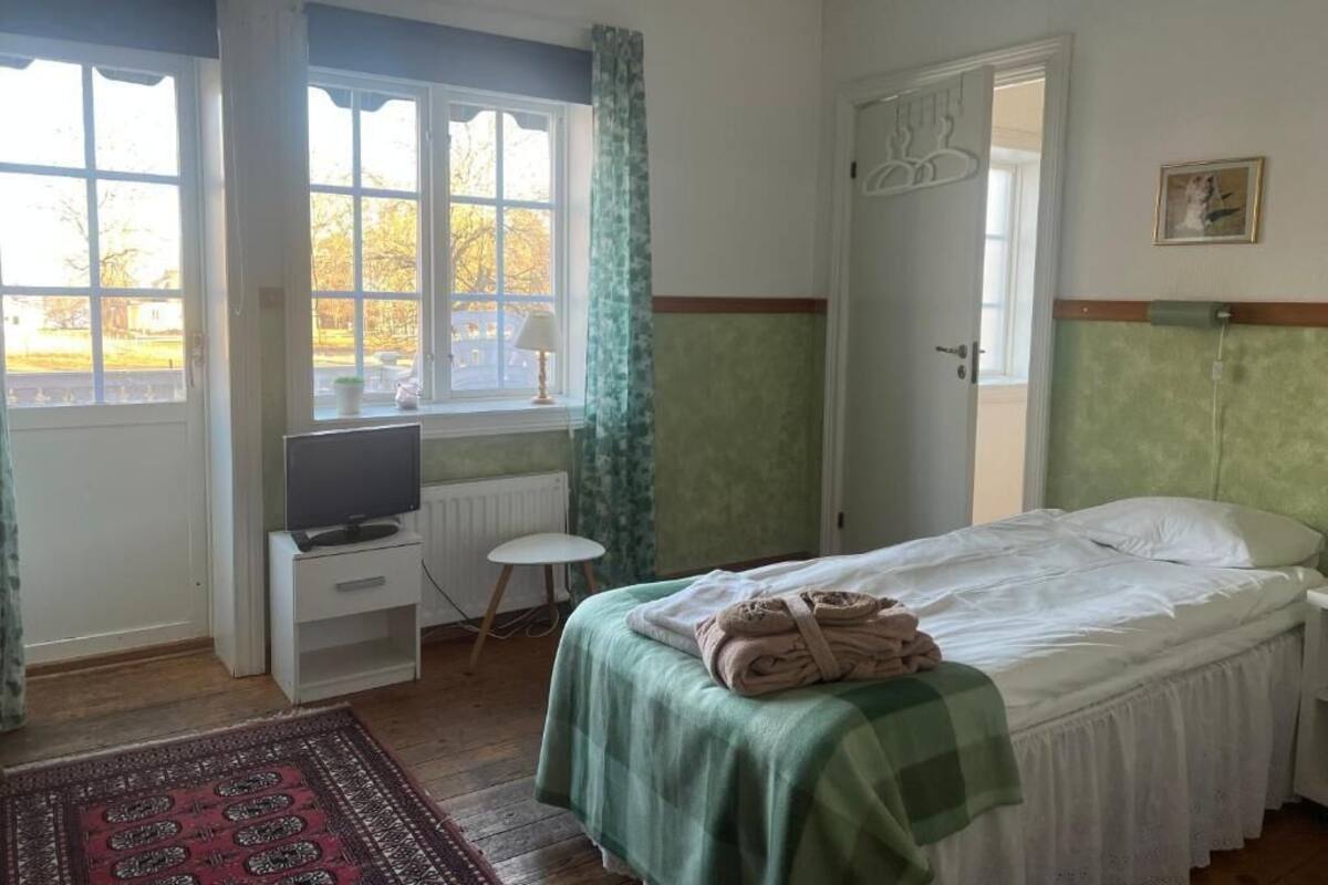 Quarto com cama, escrivaninha, cadeira, radiador e janela com cortinas.