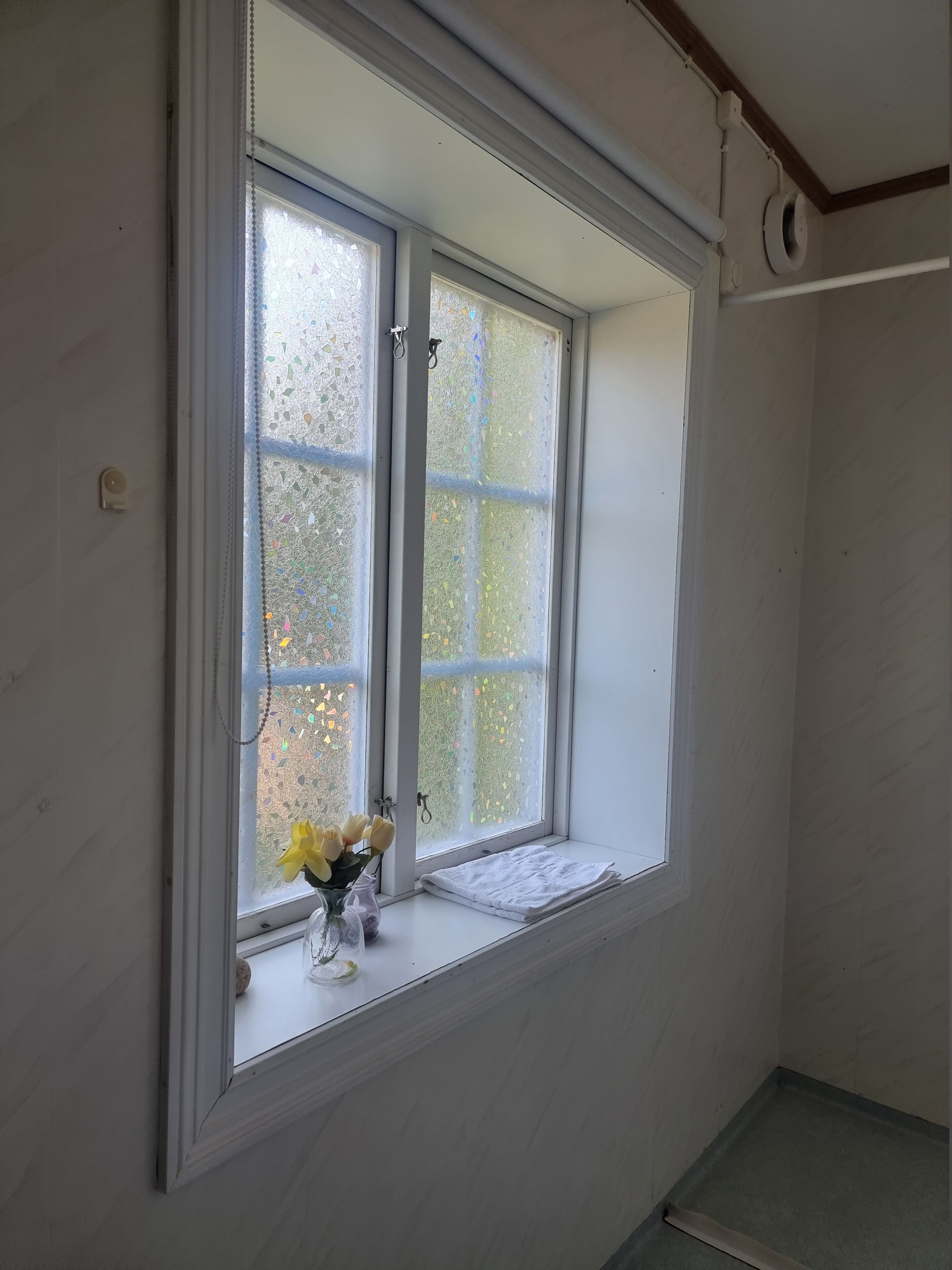 A room with a large window, a small table with a vase of flowers, and a white towel on the windowsill.
