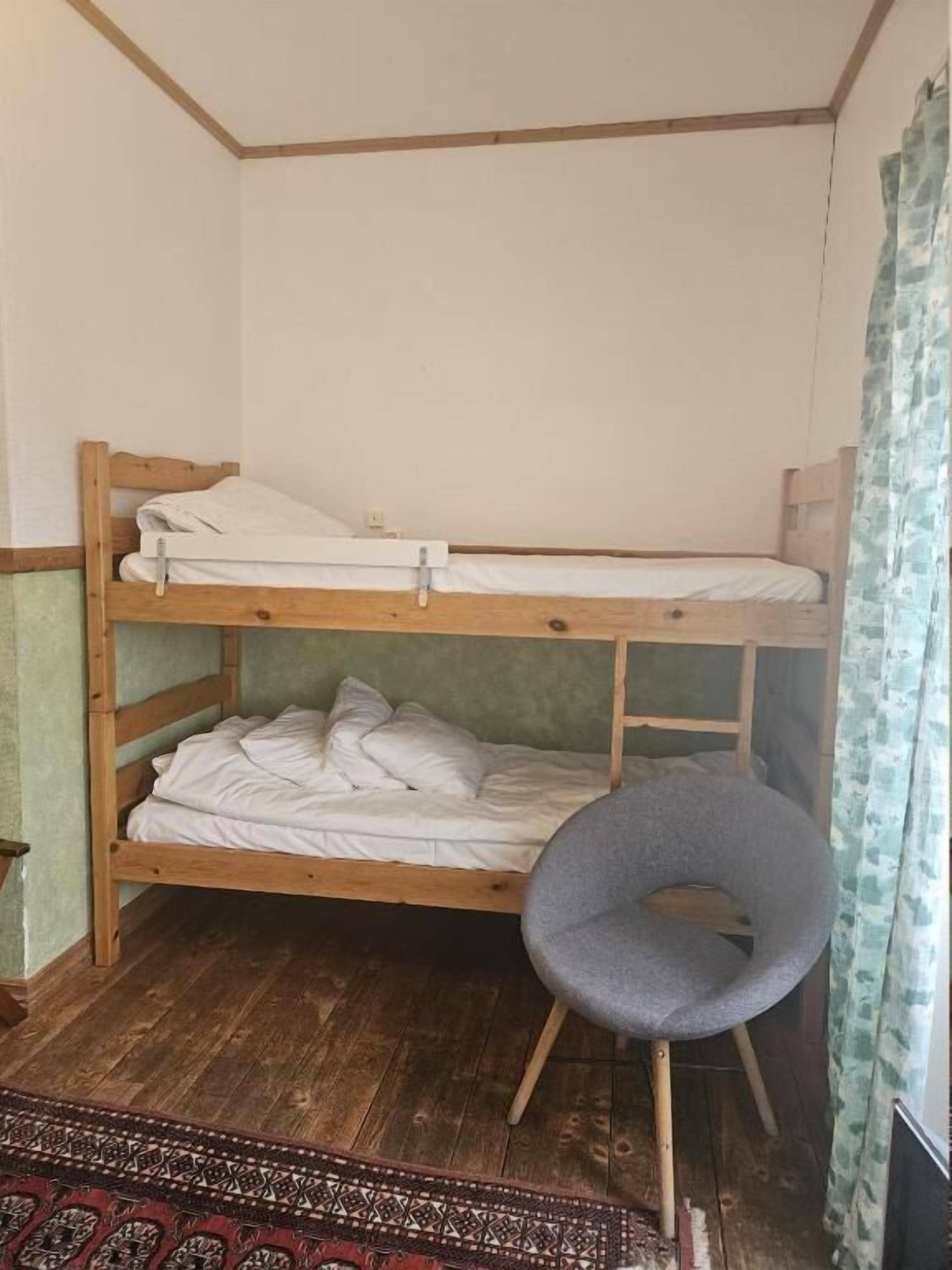 Una cama litera con una silla, suelo de madera y una alfombra estampada.