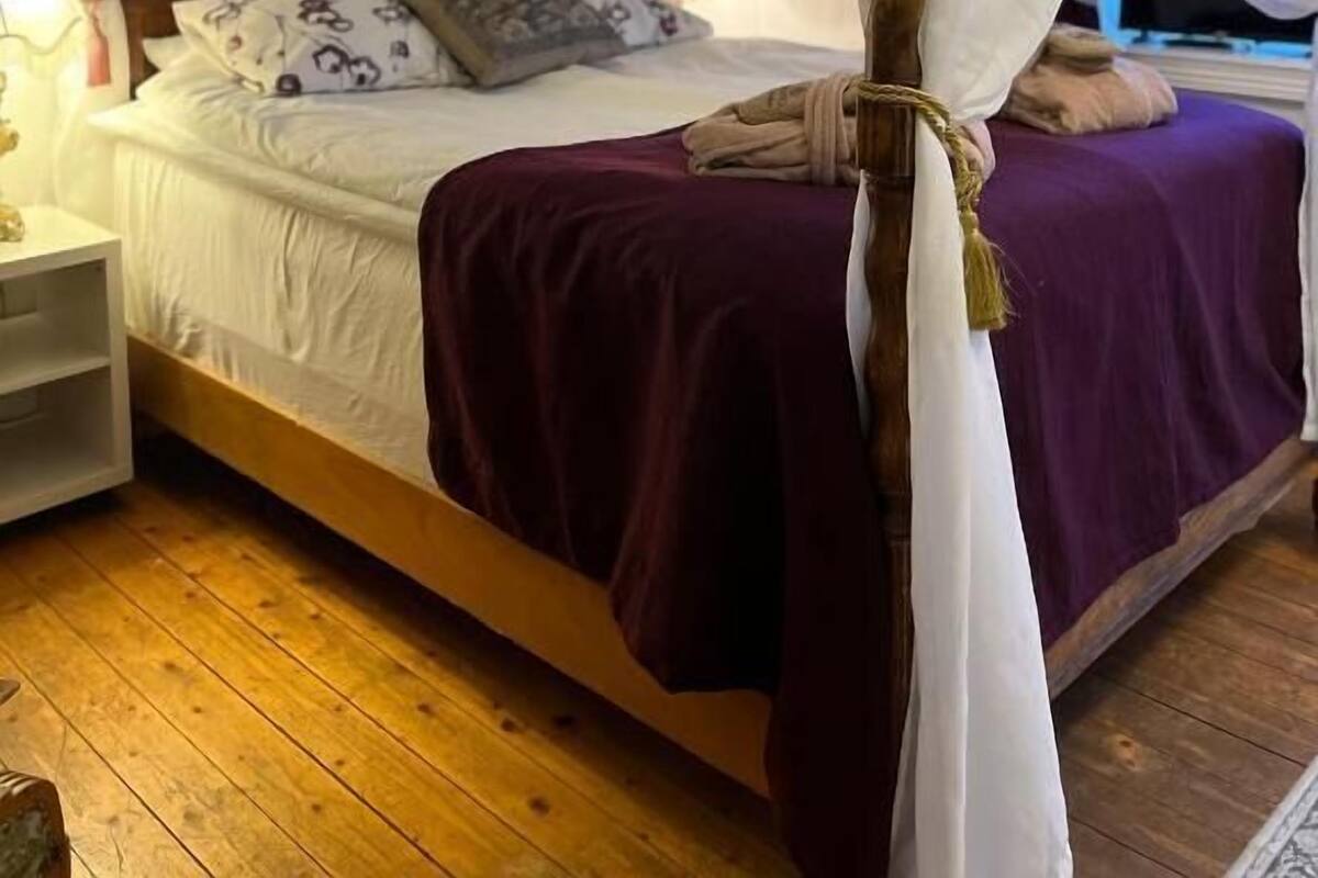 Uma cama com dossel, cabeceira de madeira e colcha roxa.