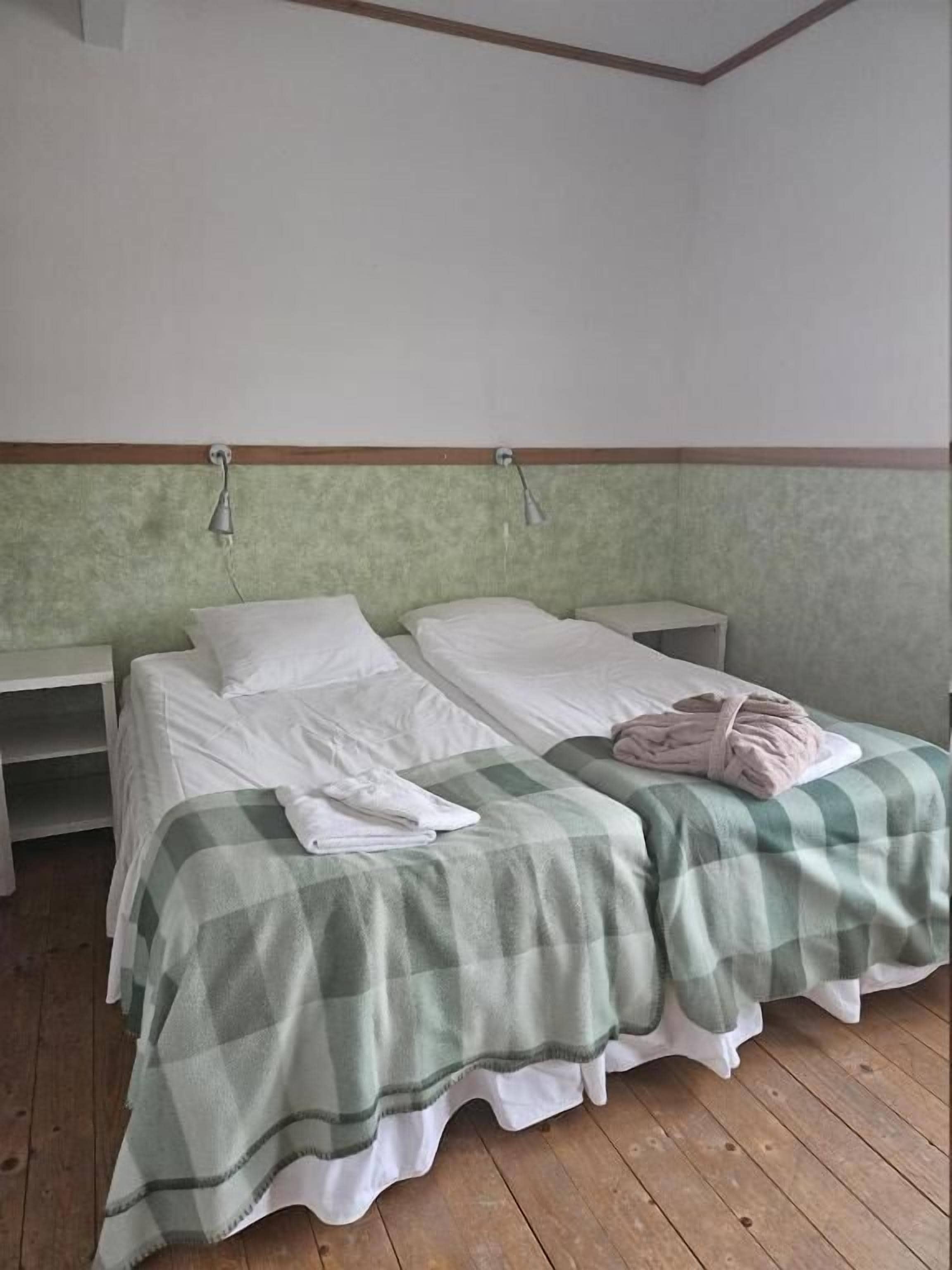 Quarto com duas camas, piso de madeira e colcha xadrez verde e branca.