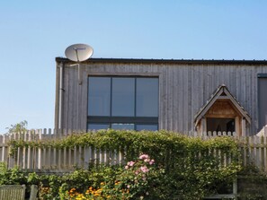 A wooden building with a satellite dish, a large window, and a small triangular entrance. - Fieldstone Barn (Okehampton)